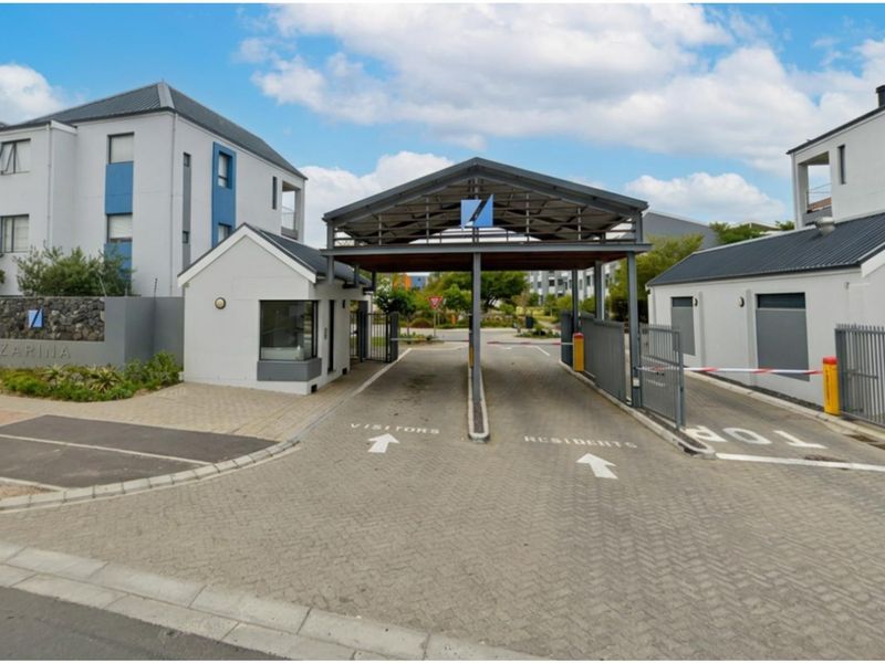 The secure entrance to the apartment complex features a dedicated gatehouse, boom-controlled access for residents and visitors, and paved driveway infrastructure.