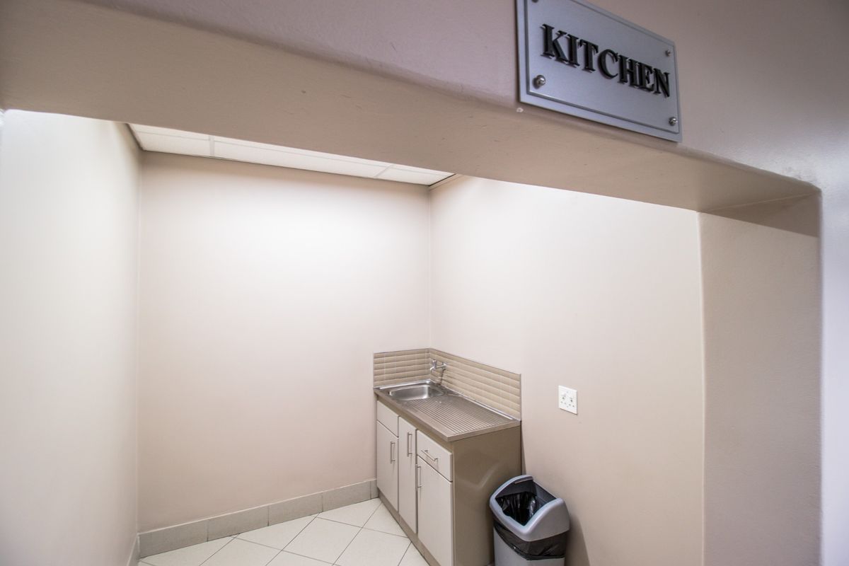 A compact commercial kitchen area featuring a stainless steel sink, tiled backsplash, and built-in cabinetry, suitable for basic food preparation or utility use.