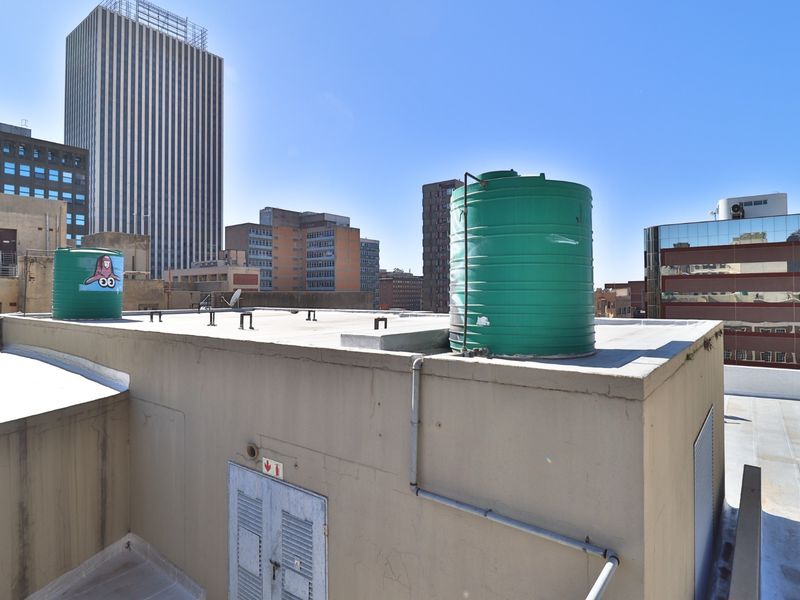 Rooftop utility area featuring two large water storage tanks and access to building infrastructure against a city skyline backdrop.