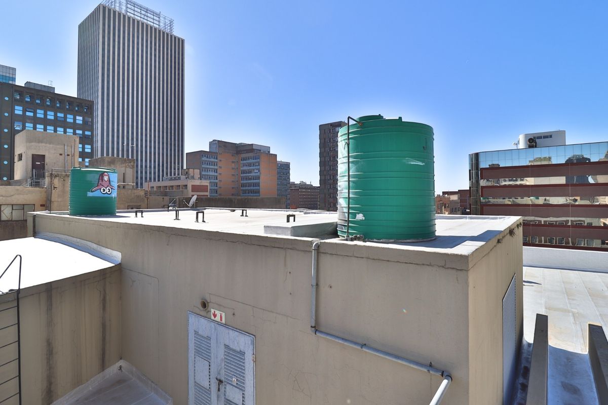 Rooftop utility area featuring two large water storage tanks and access to building infrastructure against a city skyline backdrop.