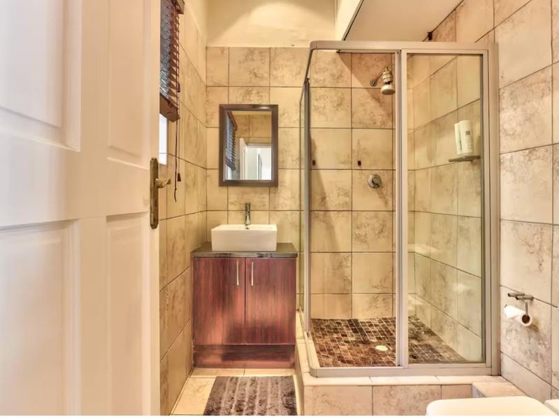A compact bathroom featuring a glass-enclosed shower, a modern vessel sink on a dark wood vanity, and neutral ceramic wall tiling.