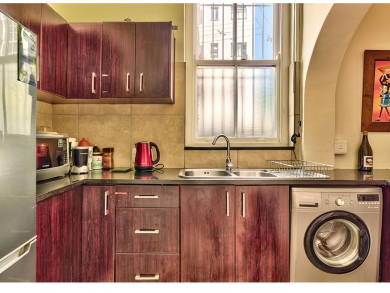 A functional kitchen featuring dark wood-look cabinetry, granite countertops, a double basin sink, and an integrated washing machine under the counter.