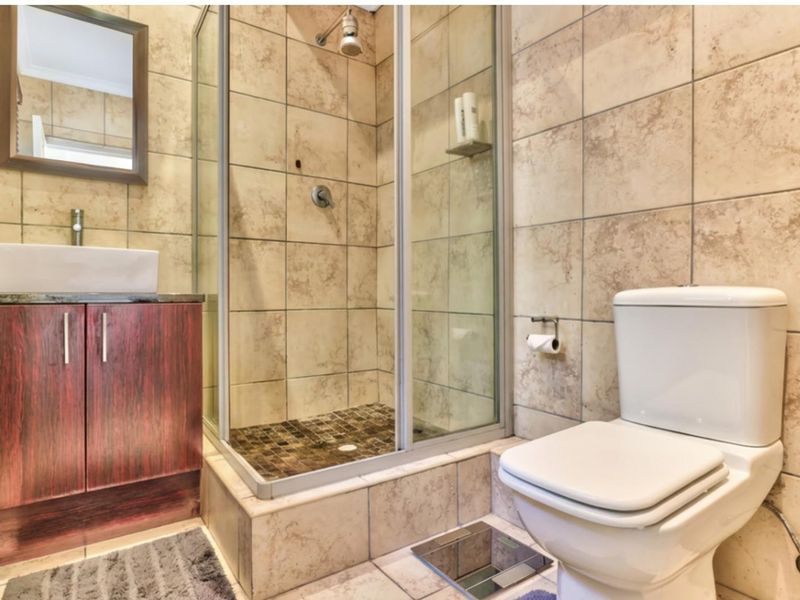 Compact bathroom featuring a shower enclosure, vanity cabinet with vessel sink, and toilet, finished with neutral wall and floor tiling.