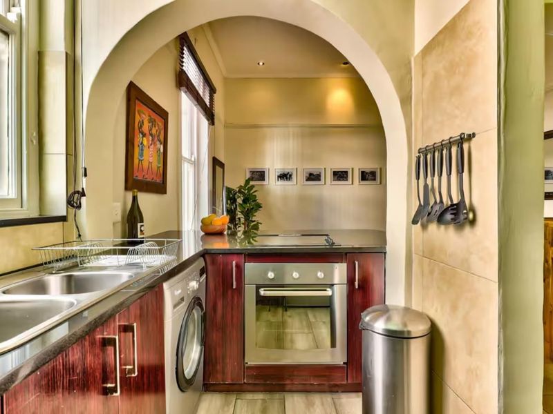 Compact kitchen featuring dark wood-finish cabinetry, stone countertops, a built-in oven, and a stainless steel sink, framed by a distinctive architectural archway.
