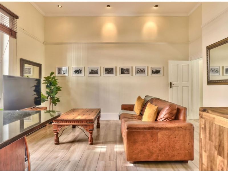 A well-maintained living room featuring high ceilings, recessed downlighting, timber-look flooring, and a classic panelled door.