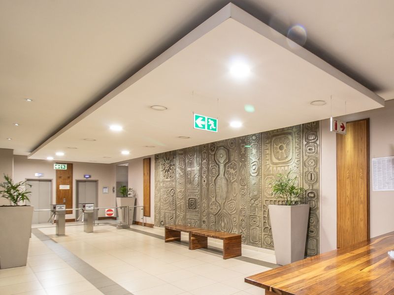 Modern commercial building lobby featuring a textured feature wall, recessed ceiling lighting, elevator access, and secure turnstile entry points.