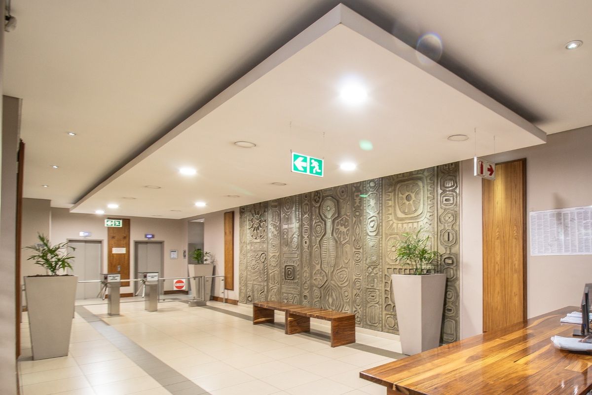 Modern commercial building lobby featuring a textured feature wall, recessed ceiling lighting, elevator access, and secure turnstile entry points.