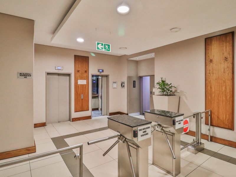 Commercial building entrance lobby featuring secure turnstile access control, elevator bank, modern tiled flooring, and professional recessed lighting.