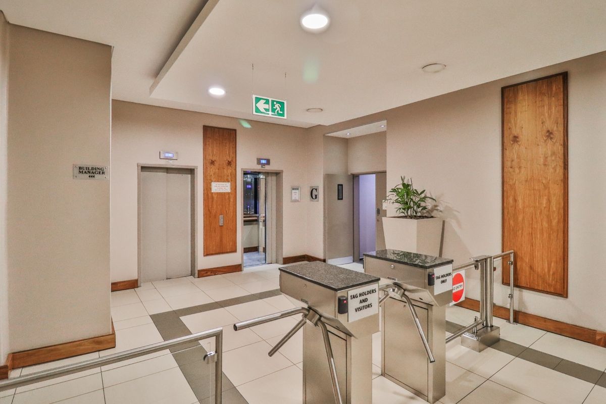 Commercial building entrance lobby featuring secure turnstile access control, elevator bank, modern tiled flooring, and professional recessed lighting.