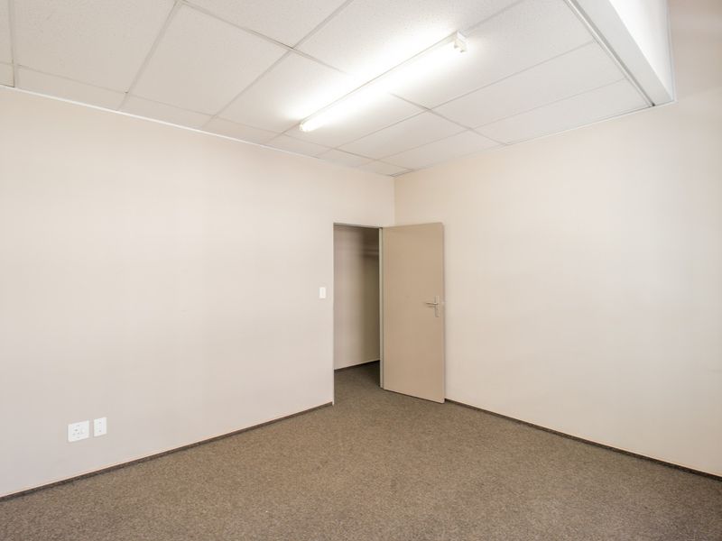 A clean, empty office space featuring neutral walls, carpeted flooring, and a suspended ceiling with integrated fluorescent lighting.