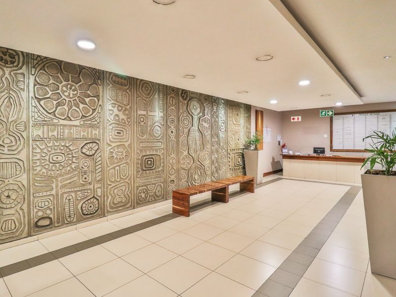 A professional commercial building lobby featuring a large decorative relief wall panel, tiled flooring, and a built-in reception desk.