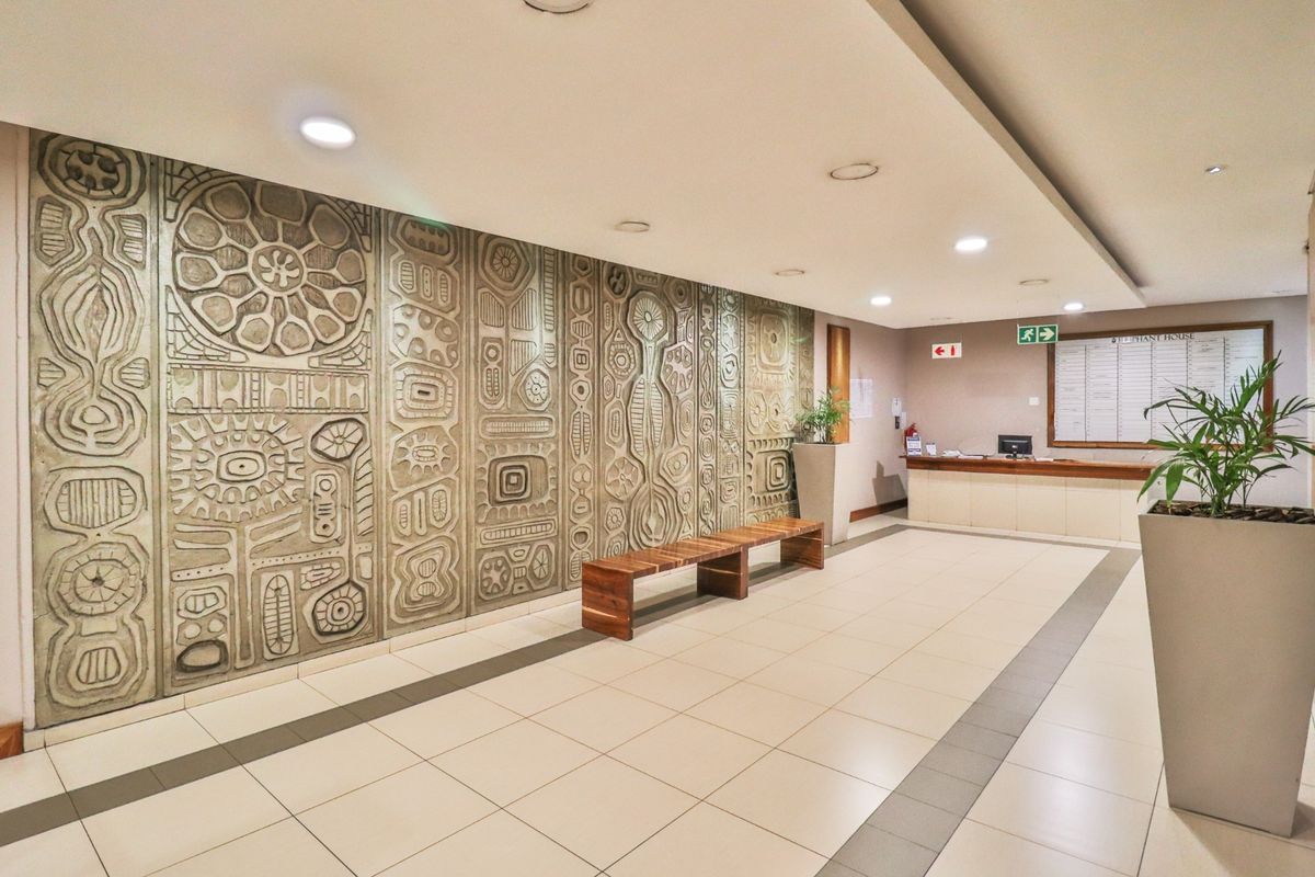 A professional commercial building lobby featuring a large decorative relief wall panel, tiled flooring, and a built-in reception desk.