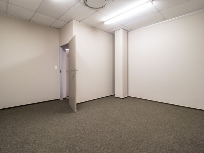 A clean, empty commercial office space featuring neutral walls, carpeted flooring, and a suspended ceiling with integrated lighting.