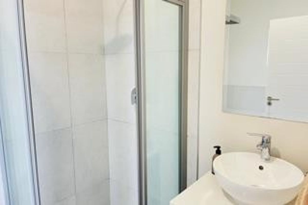 A clean, modern bathroom featuring a glass-enclosed shower, a contemporary vessel sink with a chrome faucet, and a large wall-mounted mirror.