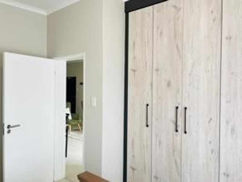 A clean bedroom interior featuring modern light wood-grain built-in cupboards and neutral wall finishes.