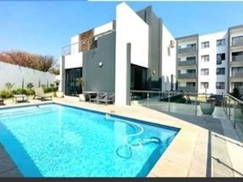Modern outdoor pool area featuring a clear swimming pool, paved decking, and glass balustrades, set against a contemporary multi-story residential building.
