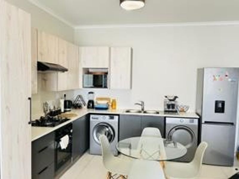 Modern open-plan kitchen featuring light wood-tone cabinetry, dark base units, integrated appliances, and a functional layout with a dedicated laundry area.