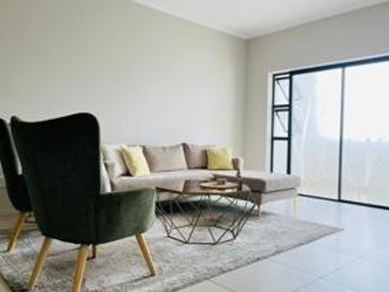 A bright and modern living room featuring neutral walls, tiled flooring, and a large sliding glass door providing access to the outdoors.