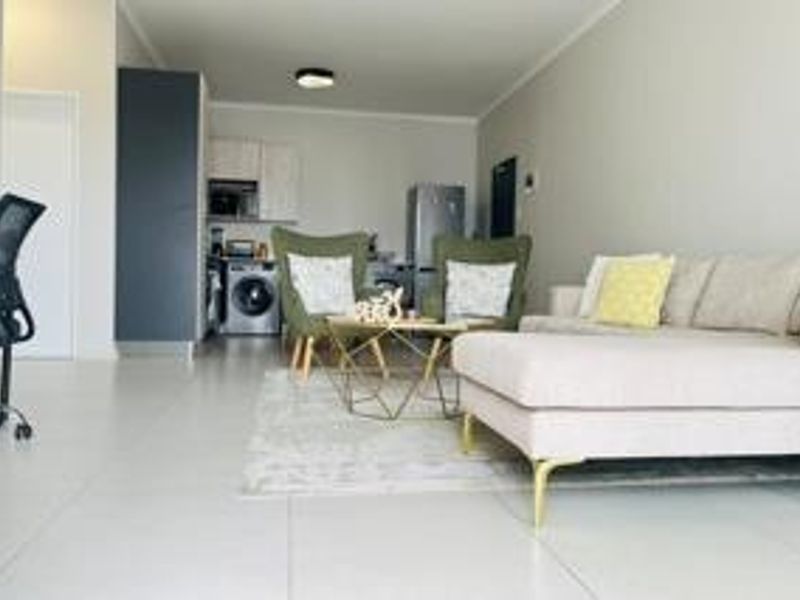 An open-plan living area featuring tiled flooring, neutral walls, and a compact kitchen space with built-in cabinetry.