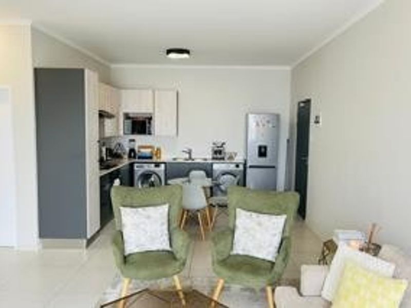 An open-plan living area featuring a modern kitchen with built-in cabinetry, integrated appliances, and tiled flooring, seamlessly flowing into the lounge space.