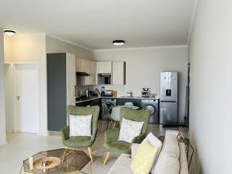 Open-plan living area featuring a modern kitchen with built-in cabinetry, integrated appliances, and tiled flooring, seamlessly flowing into the lounge space.