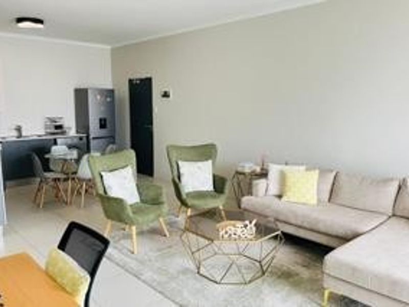 An open-plan living area featuring a compact kitchen with built-in cabinetry and a spacious lounge area with tiled flooring throughout.