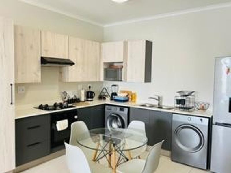 Modern kitchen featuring light wood and dark grey cabinetry, gas hob, built-in oven, microwave, and integrated laundry appliances.