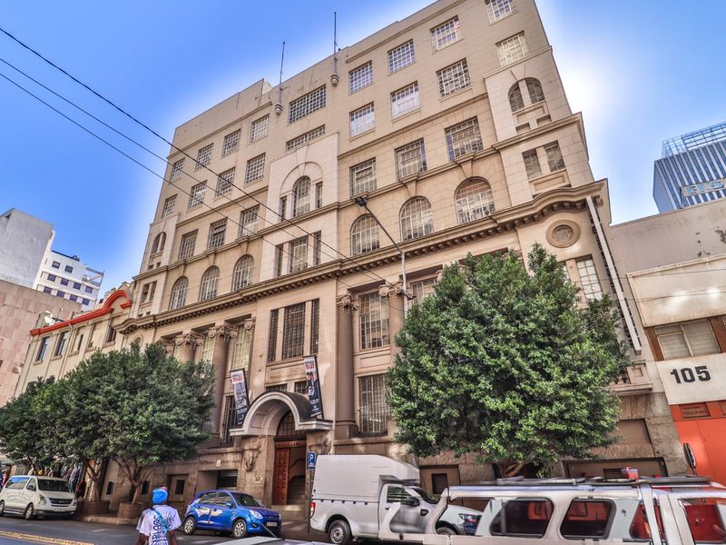 A multi-story commercial building facade featuring classical architectural elements, arched entrance, and large windows, situated in an urban street setting.