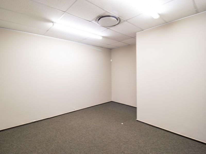 A clean, vacant office space featuring neutral walls, carpeted flooring, and a suspended ceiling with integrated lighting.