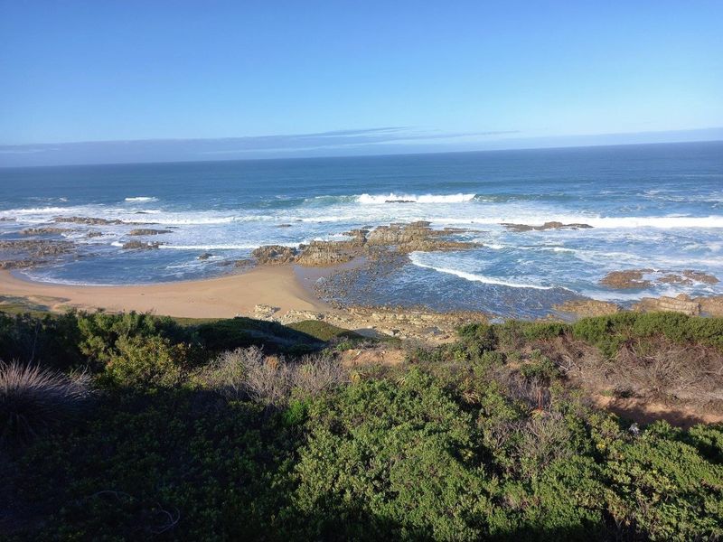 A scenic elevated view of the coastline featuring a sandy beach, rocky outcrops, and the ocean.