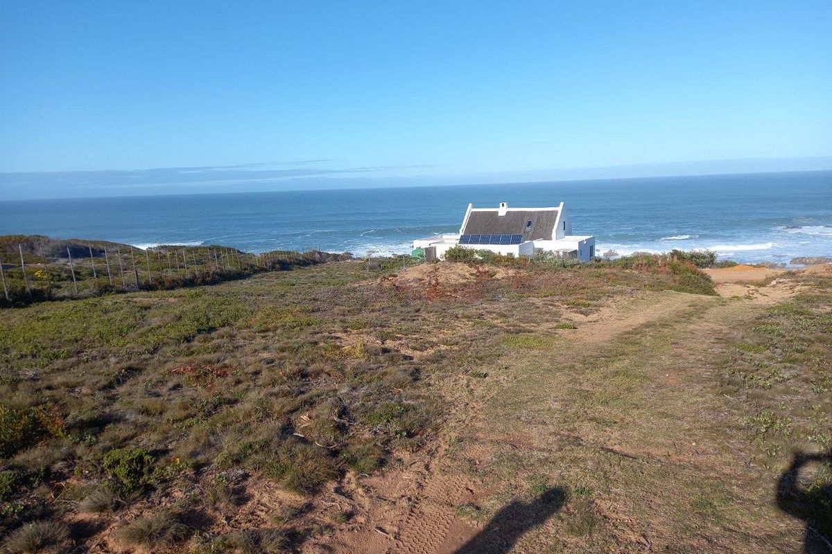 A coastal farm property featuring a white building with a thatched roof and solar panels, set against a scenic ocean backdrop.