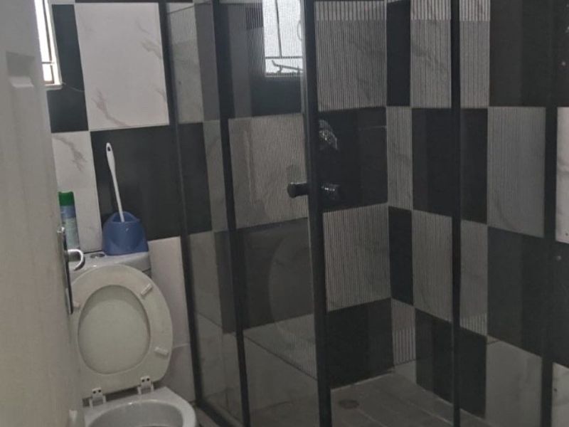 A modern bathroom featuring a corner shower enclosure with black framing and a high-contrast black and white tiled wall design.