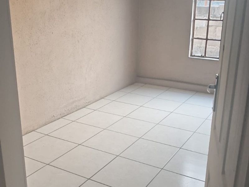 An empty bedroom featuring tiled flooring and a steel-framed window, providing a blank canvas for potential interior design and renovation.