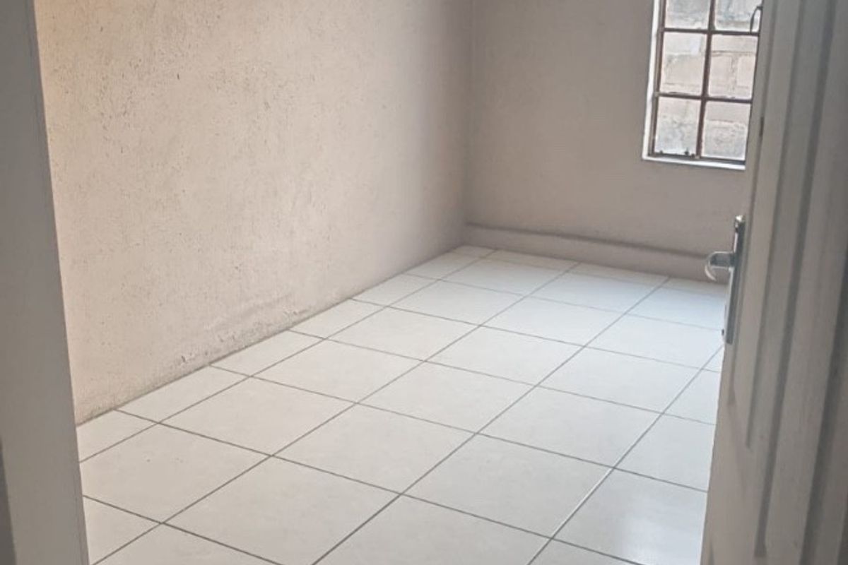 An empty bedroom featuring tiled flooring and a steel-framed window, providing a blank canvas for potential interior design and renovation.