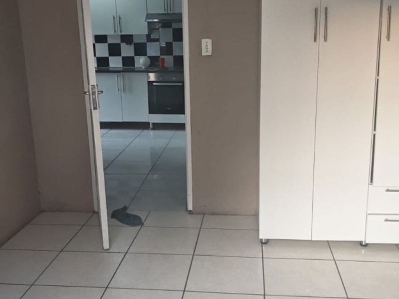 A bedroom featuring tiled flooring and a built-in wardrobe, with a view through the doorway into the adjacent kitchen area.