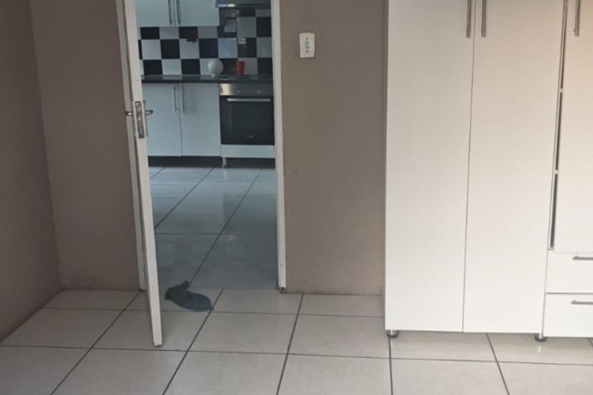 A bedroom featuring tiled flooring and a built-in wardrobe, with a view through the doorway into the adjacent kitchen area.