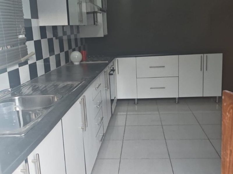 A functional kitchen featuring white cabinetry, a checkerboard backsplash, and tiled flooring. The space requires minor ceiling repairs to complete the finish.