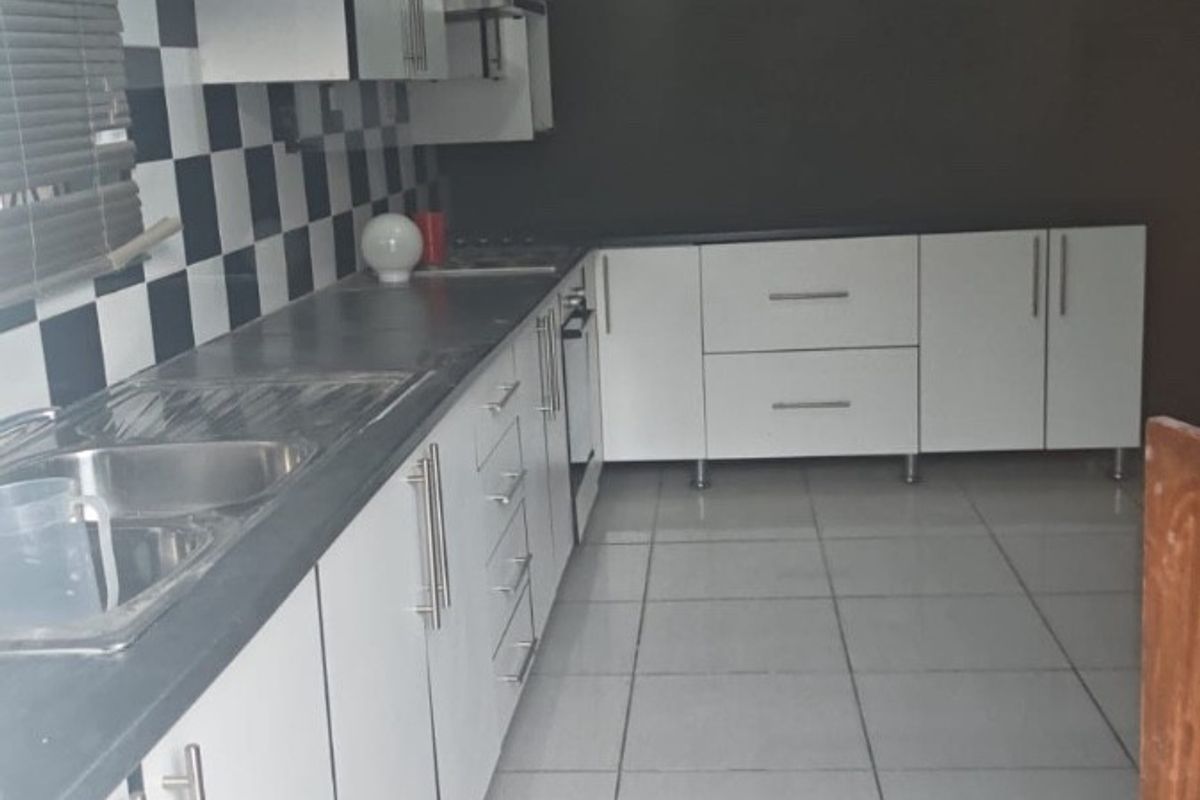 A functional kitchen featuring white cabinetry, a checkerboard backsplash, and tiled flooring. The space requires minor ceiling repairs to complete the finish.