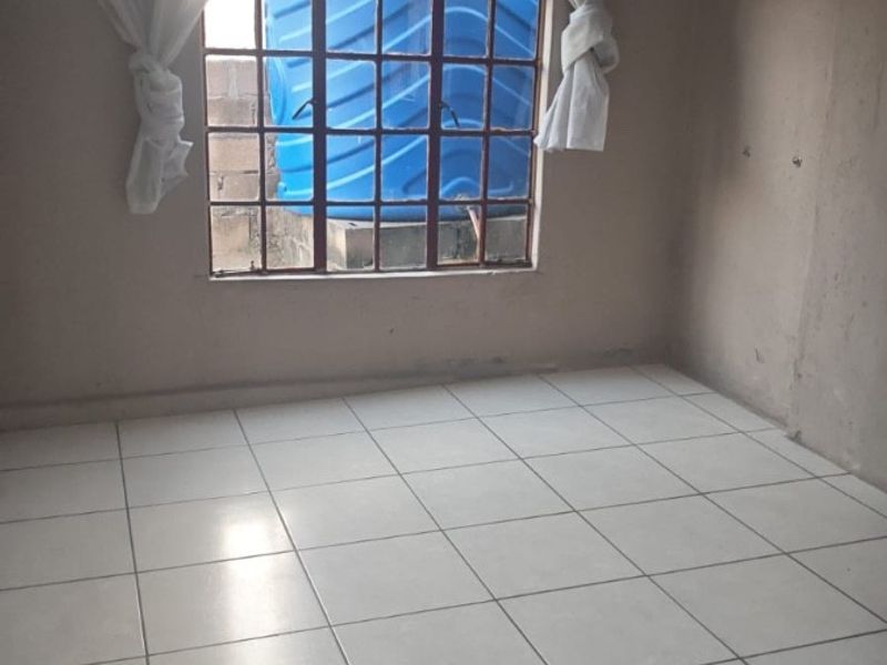 An empty bedroom featuring white tiled flooring and a steel-framed window, providing a blank canvas for potential interior design updates.