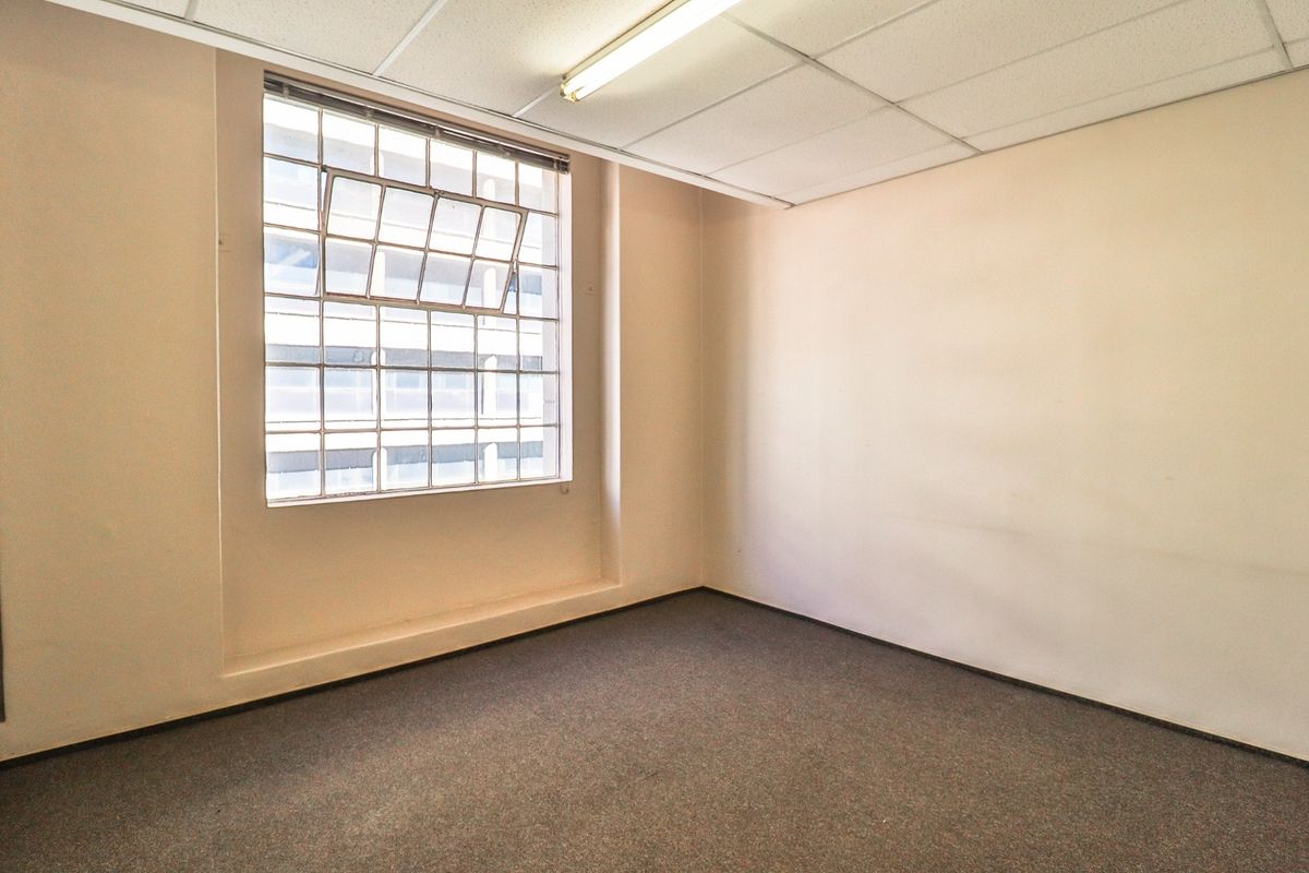 A vacant office space featuring a grid ceiling, industrial steel-framed window, and carpeted flooring, suitable for a professional workspace.
