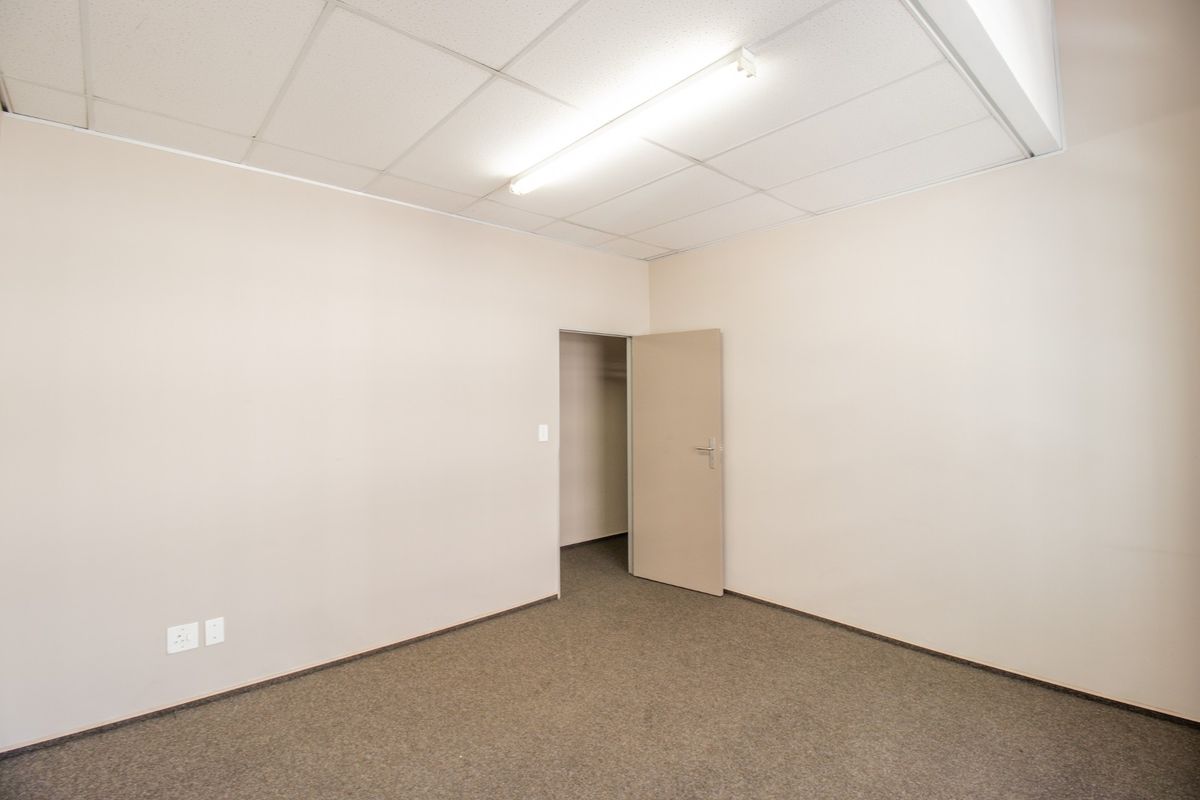 A clean, empty office space featuring neutral walls, carpeted flooring, and a suspended ceiling with integrated fluorescent lighting.