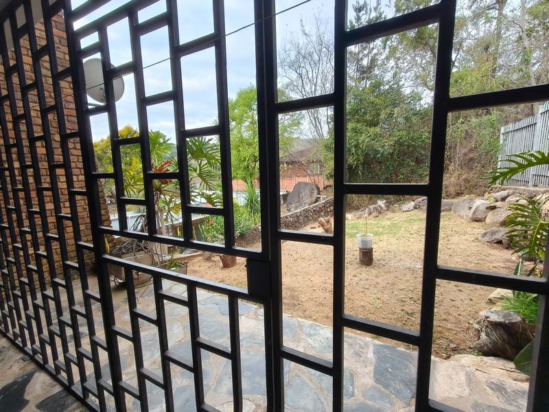 A covered patio area featuring stone flooring and a metal security gate, overlooking a private garden space.