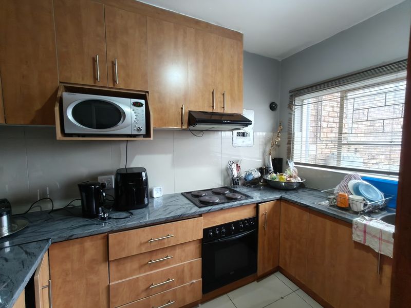 A functional kitchen featuring wood-finish cabinetry, stone-look countertops, built-in oven, hob, and extractor fan, with a tiled backsplash and window with blinds.