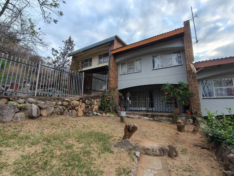 Rear view of a multi-level townhouse featuring a brick and rendered facade, security fencing, and a tiered garden area with stone retaining walls.