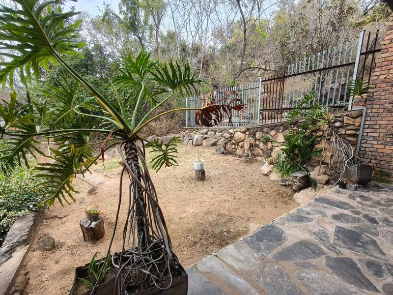 Rear garden area featuring a stone retaining wall, metal security fencing, and flagstone patio paving, requiring landscaping and maintenance.
