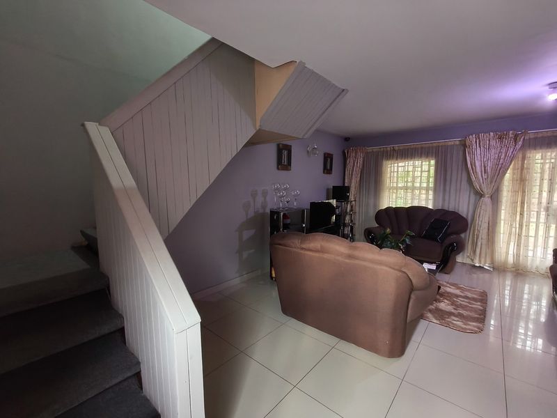 A living room featuring tiled flooring, a staircase with wooden paneling, and a sliding glass door providing access to the exterior.