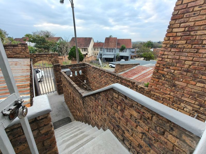 An elevated view of a brick staircase leading to a rear courtyard area with surrounding brick boundary walls and metal security gate.