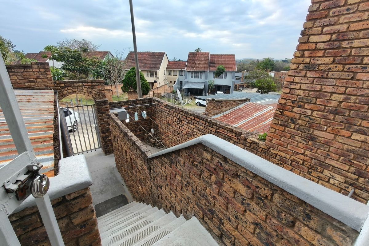 An elevated view of a brick staircase leading to a rear courtyard area with surrounding brick boundary walls and metal security gate.