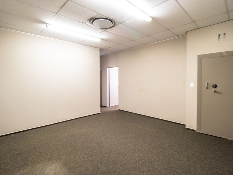 A vacant commercial office space featuring neutral walls, carpeted flooring, suspended ceiling lighting, and a secure heavy-duty steel vault door.