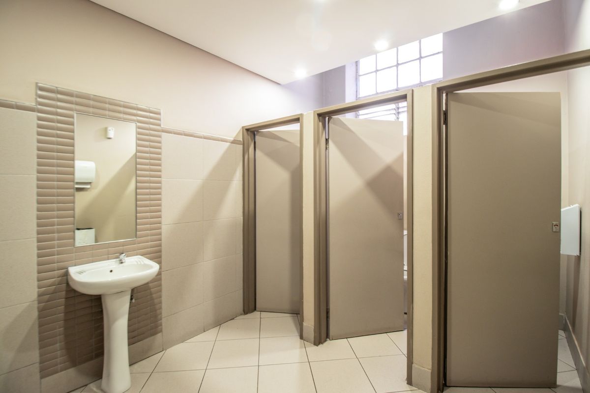 A clean and well-maintained commercial restroom featuring a pedestal washbasin, tiled walls and floors, and multiple private cubicles.
